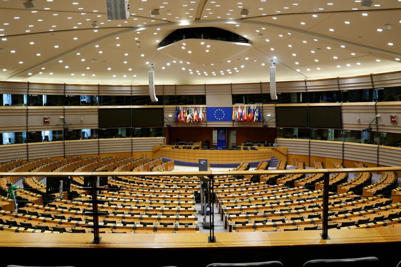 Empty plenary chamber of the European Parliament with EU member-state flags at the central podium.